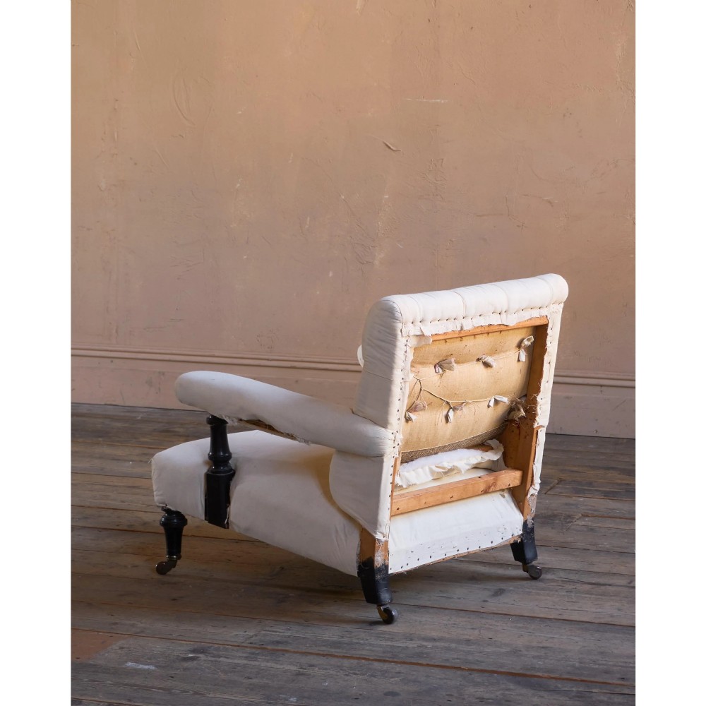 An antique Victorian open armchair upholstered in off-white calico fabric featuring a deep-buttoned backrest, padded arms, turned dark timber supports, and legs on castors. View IV