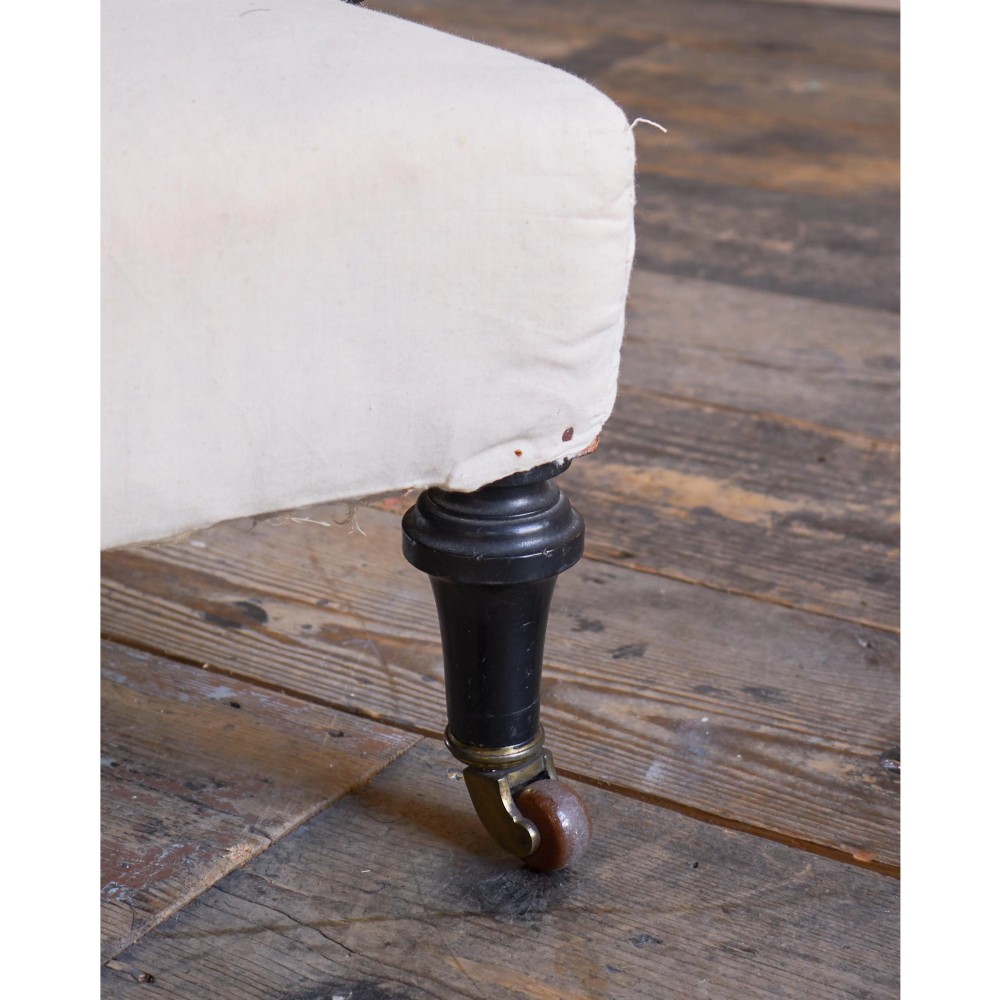 An antique Victorian open armchair upholstered in off-white calico fabric featuring a deep-buttoned backrest, padded arms, turned dark timber supports, and legs on castors. View V