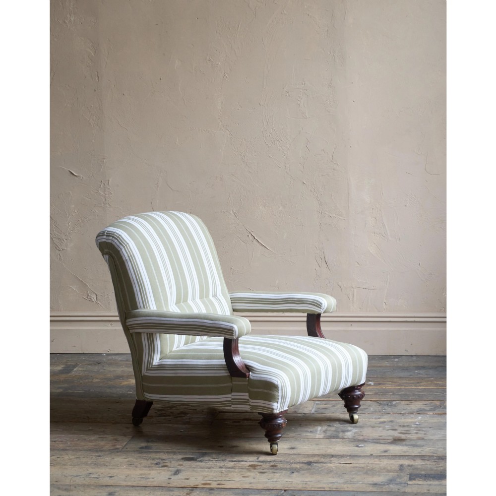 An oversized 19th-century open armchair upholstered in sage green and white striped fabric with carved mahogany arm supports and turned legs on brass castors. View III