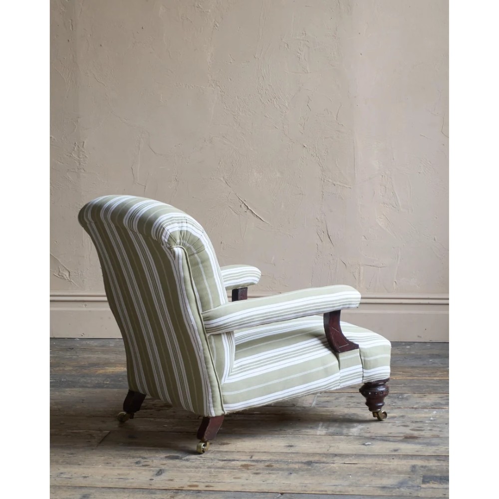 An oversized 19th-century open armchair upholstered in sage green and white striped fabric with carved mahogany arm supports and turned legs on brass castors. View IV
