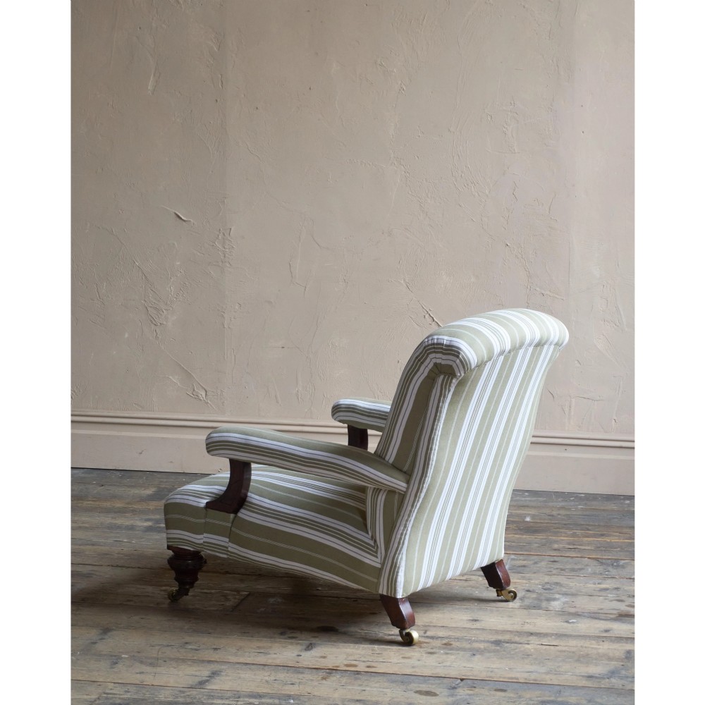 An oversized 19th-century open armchair upholstered in sage green and white striped fabric with carved mahogany arm supports and turned legs on brass castors. View V