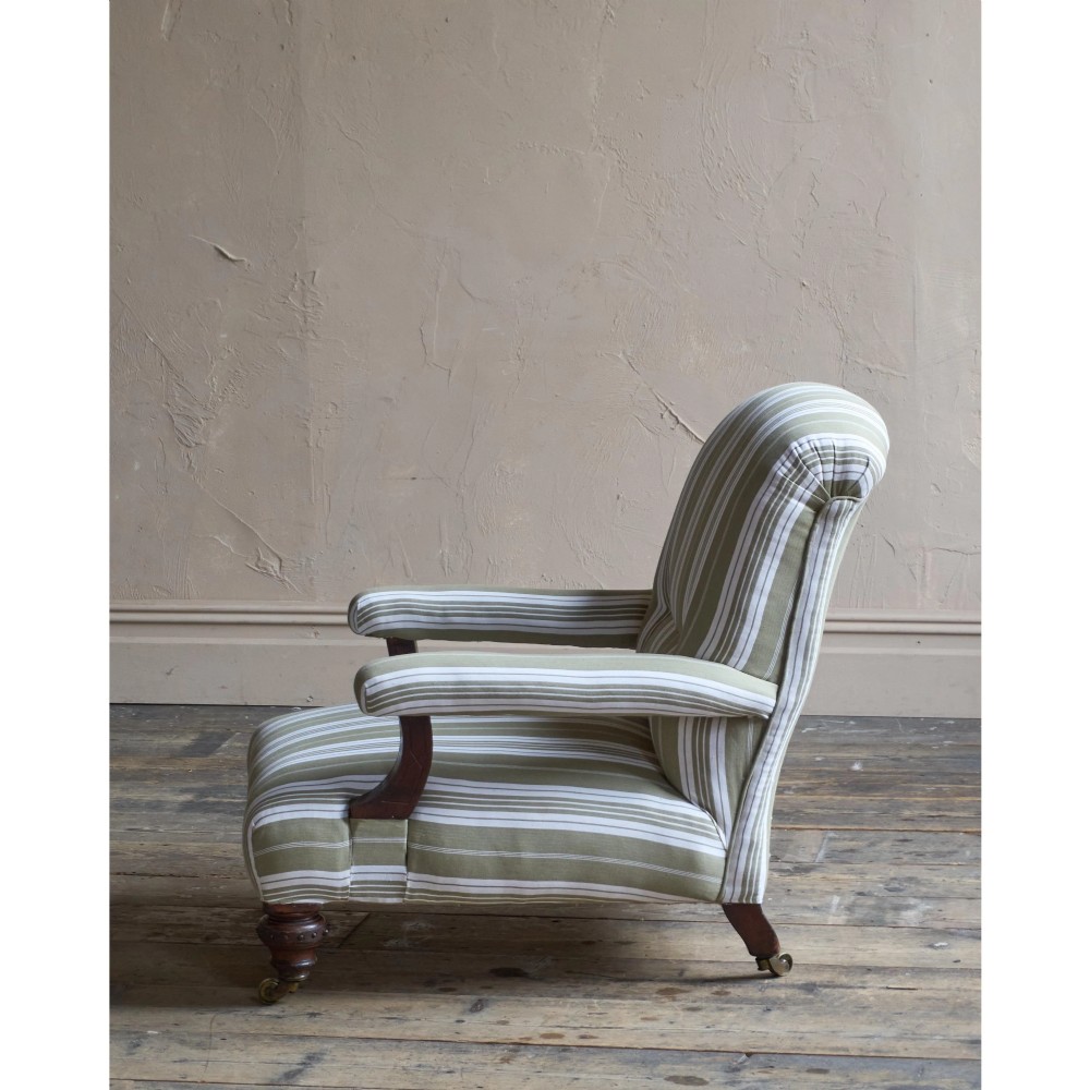 An oversized 19th-century open armchair upholstered in sage green and white striped fabric with carved mahogany arm supports and turned legs on brass castors. View VI