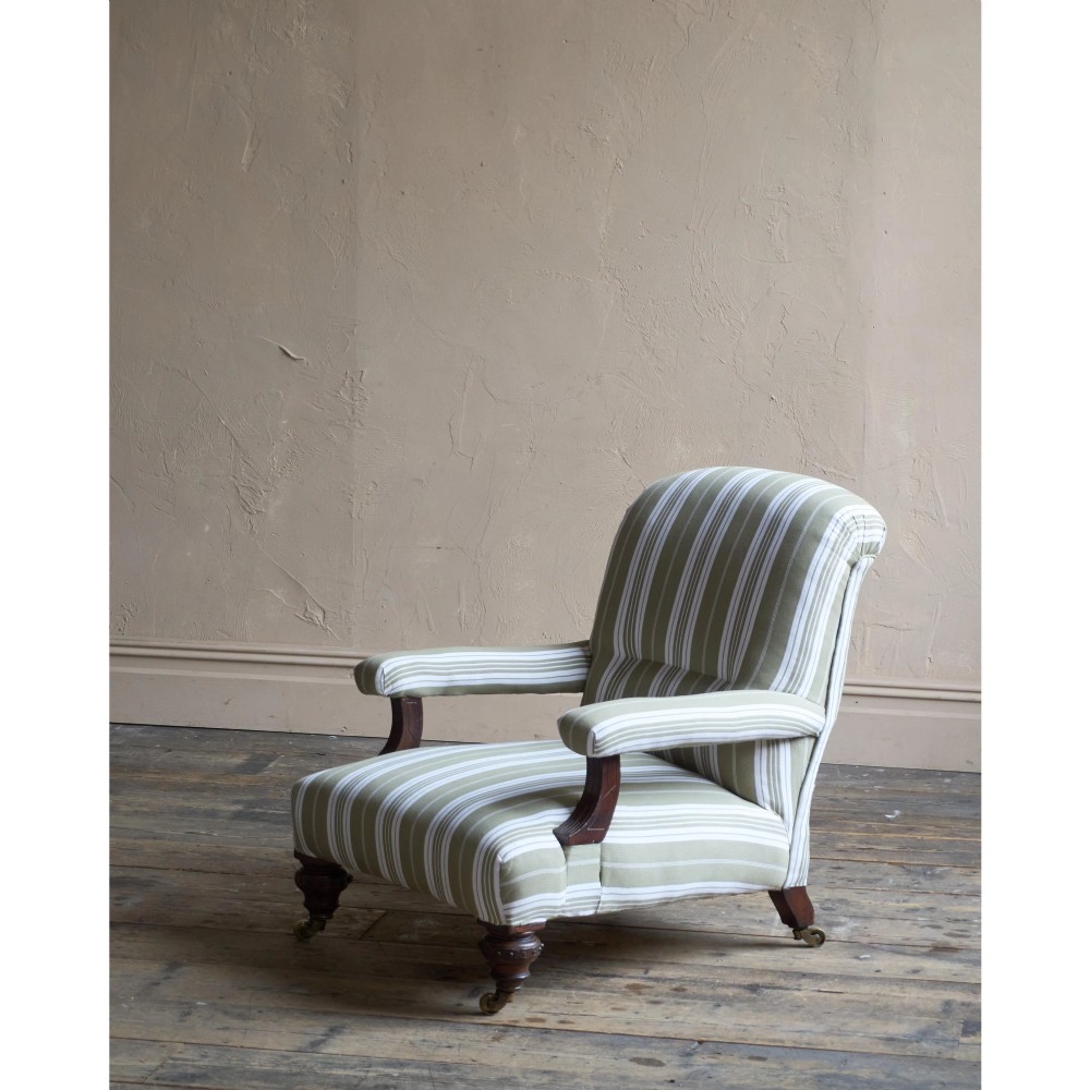 An oversized 19th-century open armchair upholstered in sage green and white striped fabric with carved mahogany arm supports and turned legs on brass castors. View VII