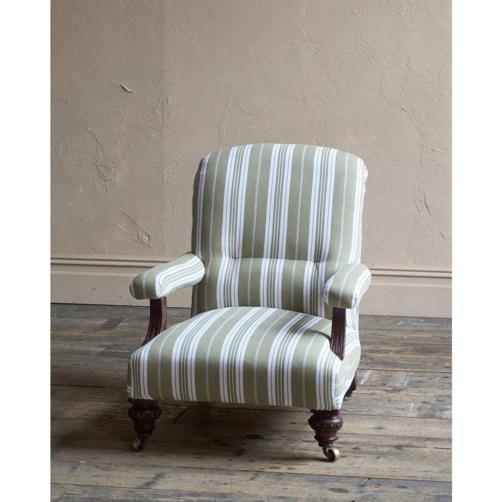 An oversized 19th-century open armchair upholstered in sage green and white striped fabric with carved mahogany arm supports and turned legs on brass castors. View VIII