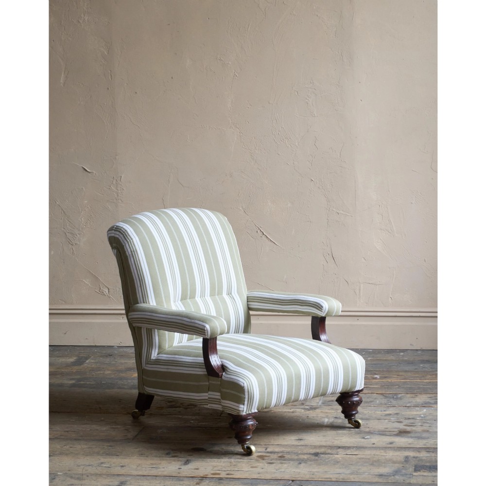 An oversized 19th-century open armchair upholstered in sage green and white striped fabric with carved mahogany arm supports and turned legs on brass castors. View IX