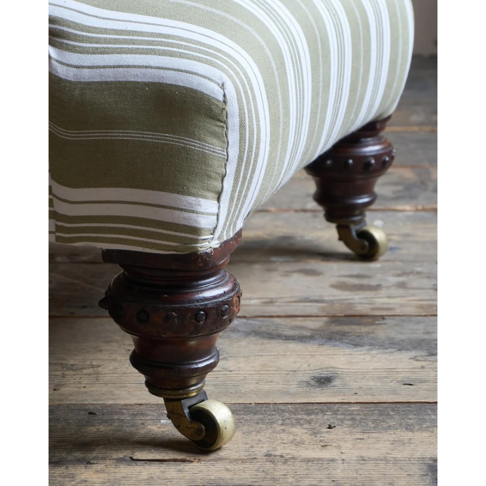 An oversized 19th-century open armchair upholstered in sage green and white striped fabric with carved mahogany arm supports and turned legs on brass castors. View X