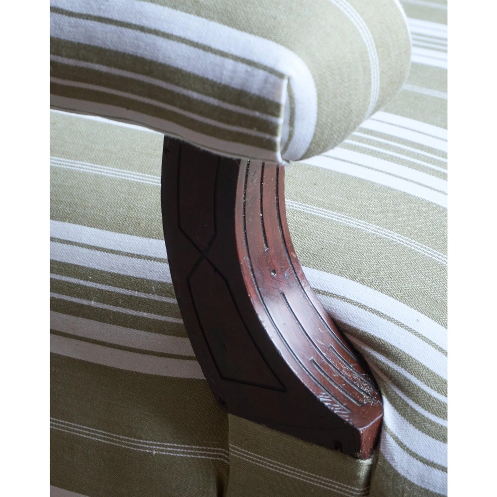 An oversized 19th-century open armchair upholstered in sage green and white striped fabric with carved mahogany arm supports and turned legs on brass castors. View XI