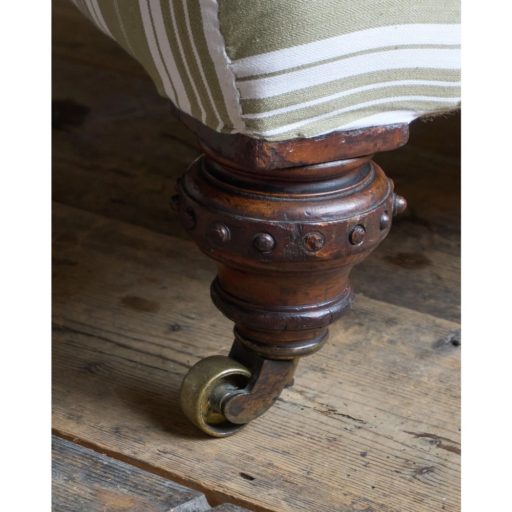 An oversized 19th-century open armchair upholstered in sage green and white striped fabric with carved mahogany arm supports and turned legs on brass castors. View XII