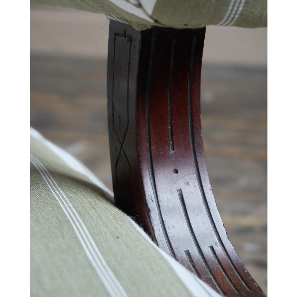 An oversized 19th-century open armchair upholstered in sage green and white striped fabric with carved mahogany arm supports and turned legs on brass castors. View XIII