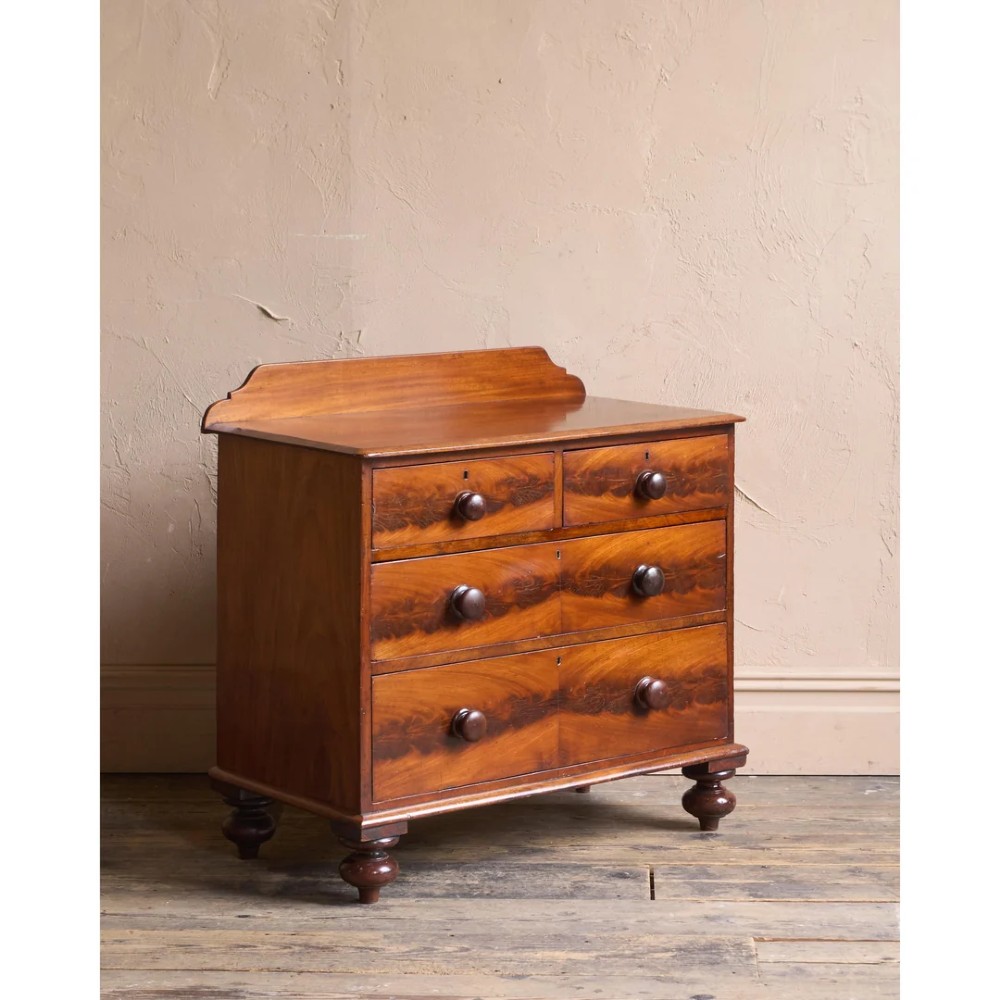 A nineteenth-century warm brown mahogany chest of drawers featuring flame mahogany veneer, turned handles, and a shaped gallery top.