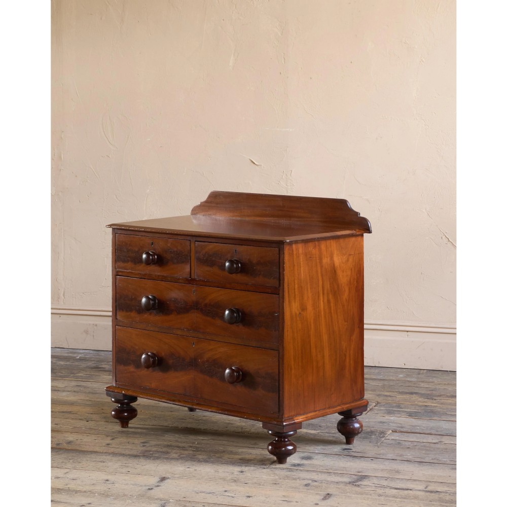 A nineteenth-century warm brown mahogany chest of drawers featuring flame mahogany veneer, turned handles, and a shaped gallery top. View II