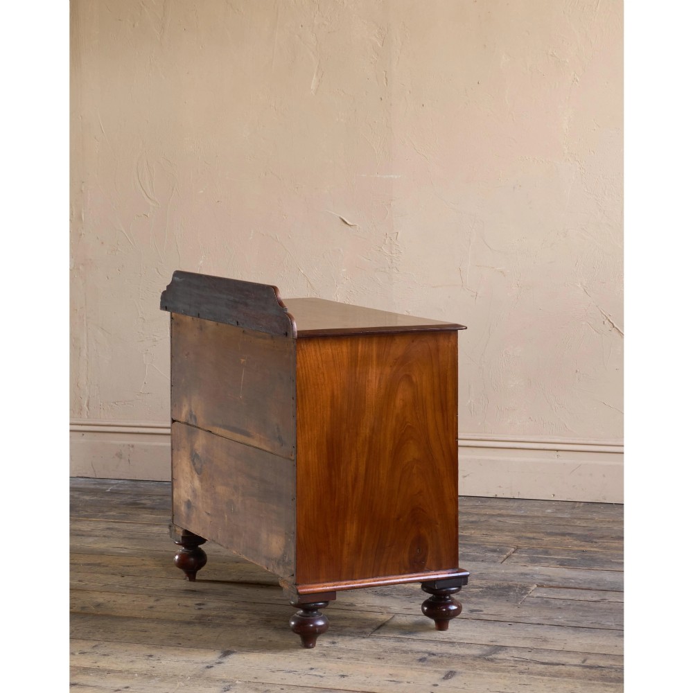 A nineteenth-century warm brown mahogany chest of drawers featuring flame mahogany veneer, turned handles, and a shaped gallery top. View IV