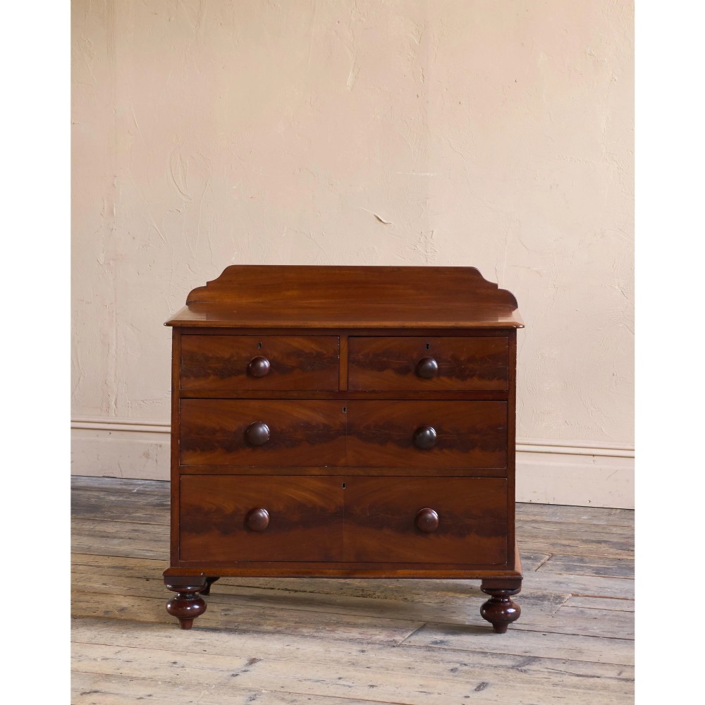 A nineteenth-century warm brown mahogany chest of drawers featuring flame mahogany veneer, turned handles, and a shaped gallery top. View V