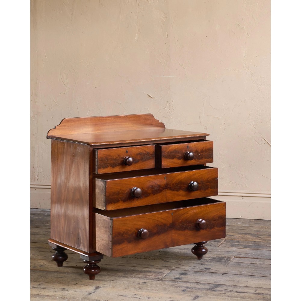 A nineteenth-century warm brown mahogany chest of drawers featuring flame mahogany veneer, turned handles, and a shaped gallery top. View VI