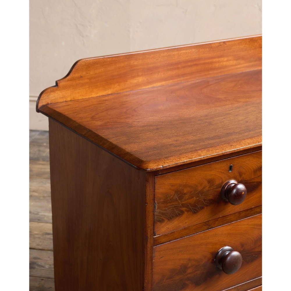A nineteenth-century warm brown mahogany chest of drawers featuring flame mahogany veneer, turned handles, and a shaped gallery top. View VII