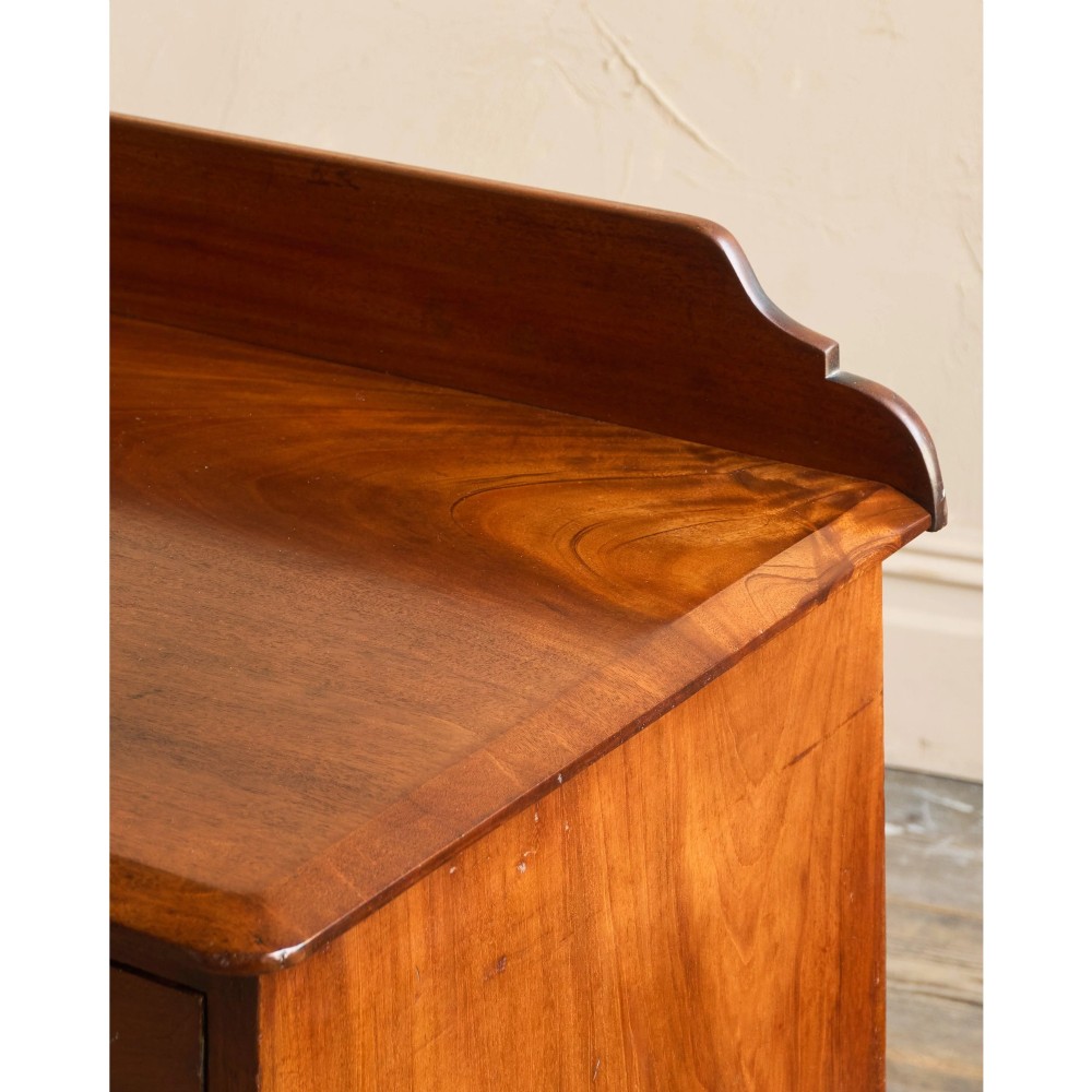 A nineteenth-century warm brown mahogany chest of drawers featuring flame mahogany veneer, turned handles, and a shaped gallery top. View IX