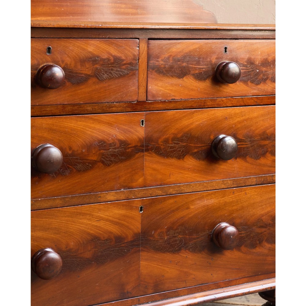 A nineteenth-century warm brown mahogany chest of drawers featuring flame mahogany veneer, turned handles, and a shaped gallery top. View X