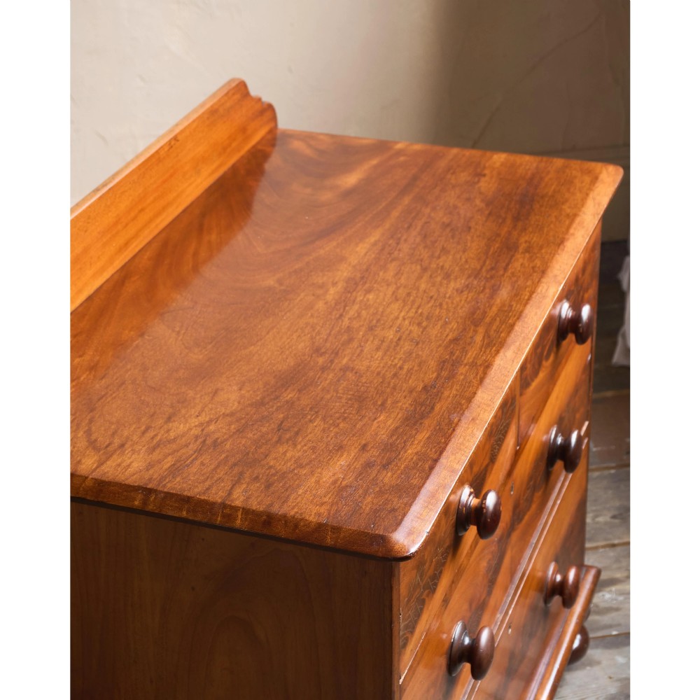A nineteenth-century warm brown mahogany chest of drawers featuring flame mahogany veneer, turned handles, and a shaped gallery top. View XII