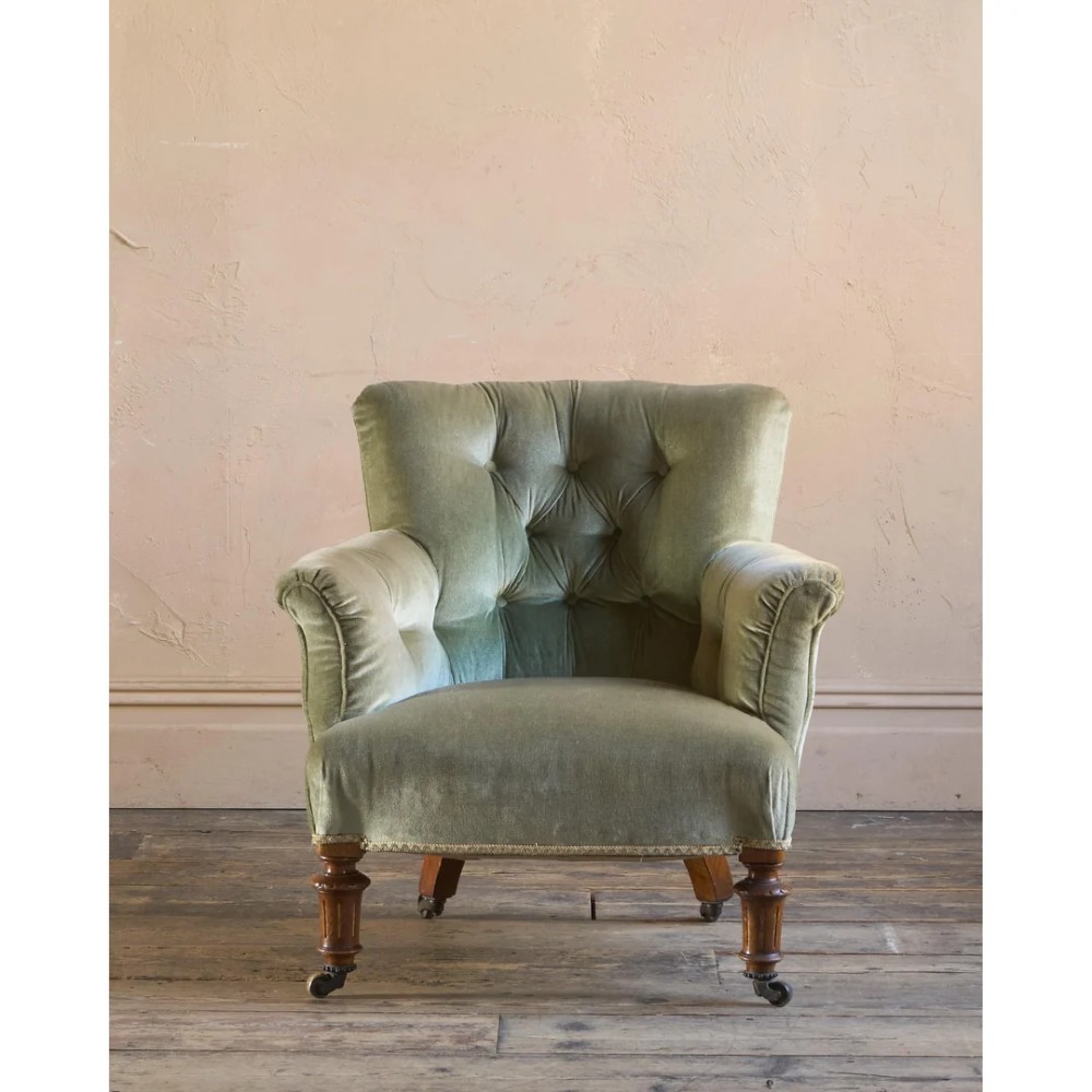 A 19th-century Victorian low armchair upholstered in light sage green velvet with a button-back design and turned wooden front legs on brass castors. View II