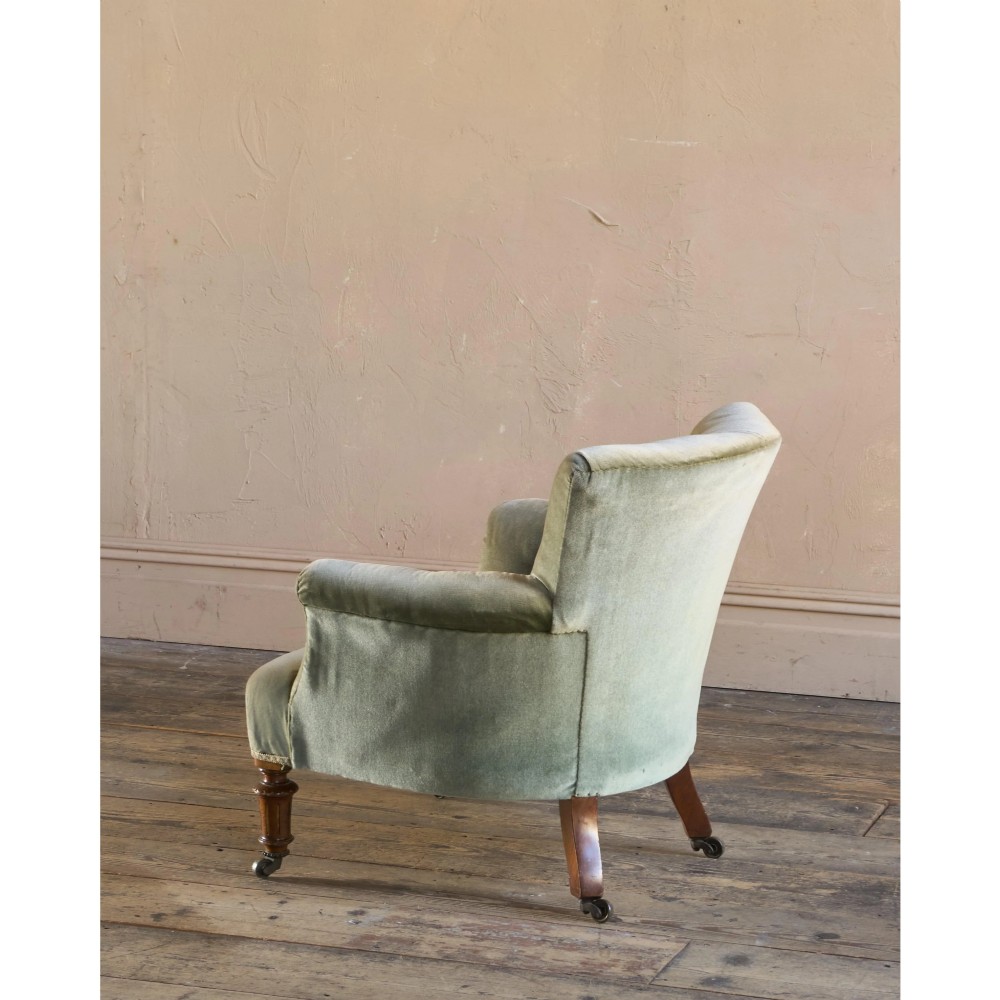 A 19th-century Victorian low armchair upholstered in light sage green velvet with a button-back design and turned wooden front legs on brass castors. View III
