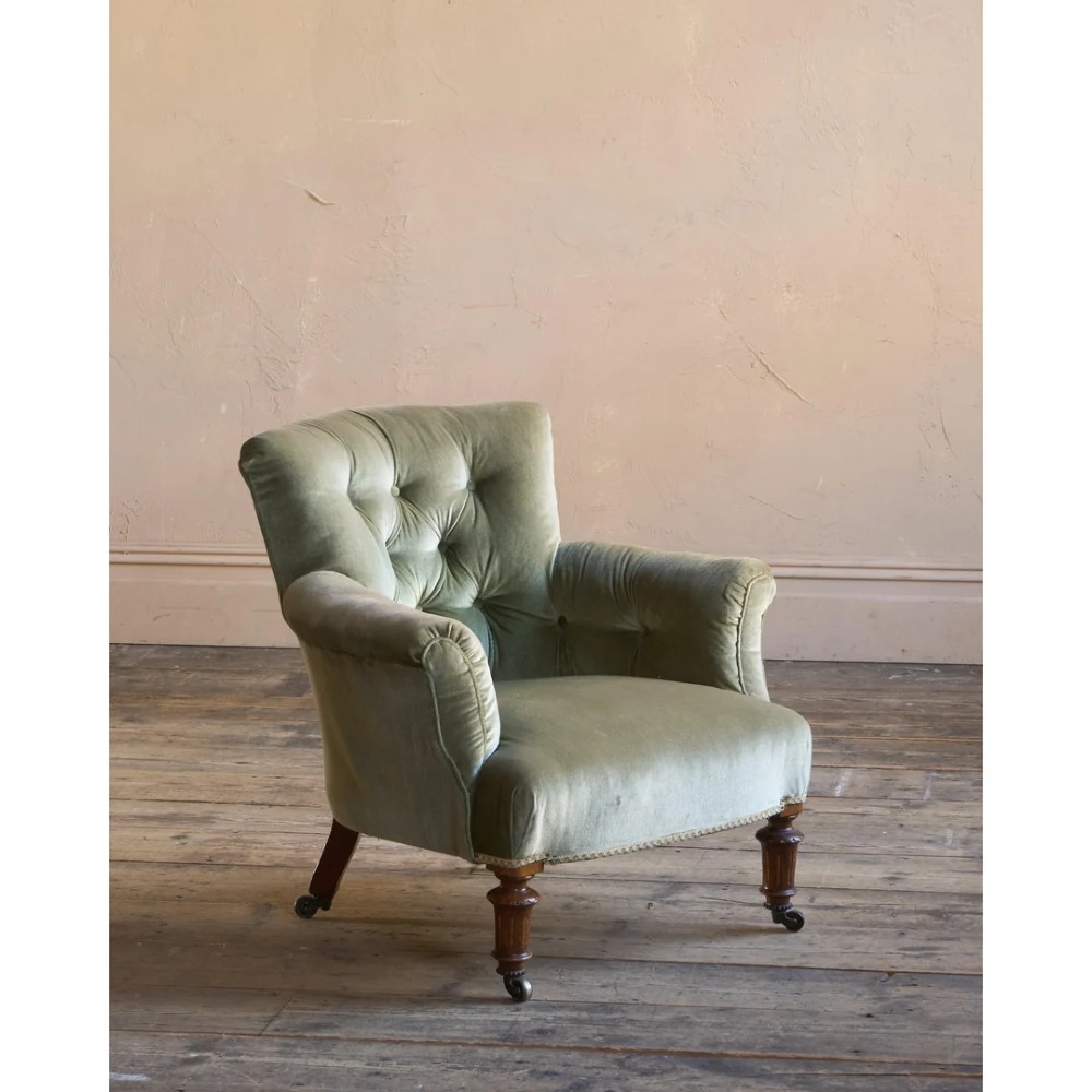 A 19th-century Victorian low armchair upholstered in light sage green velvet with a button-back design and turned wooden front legs on brass castors. View IV