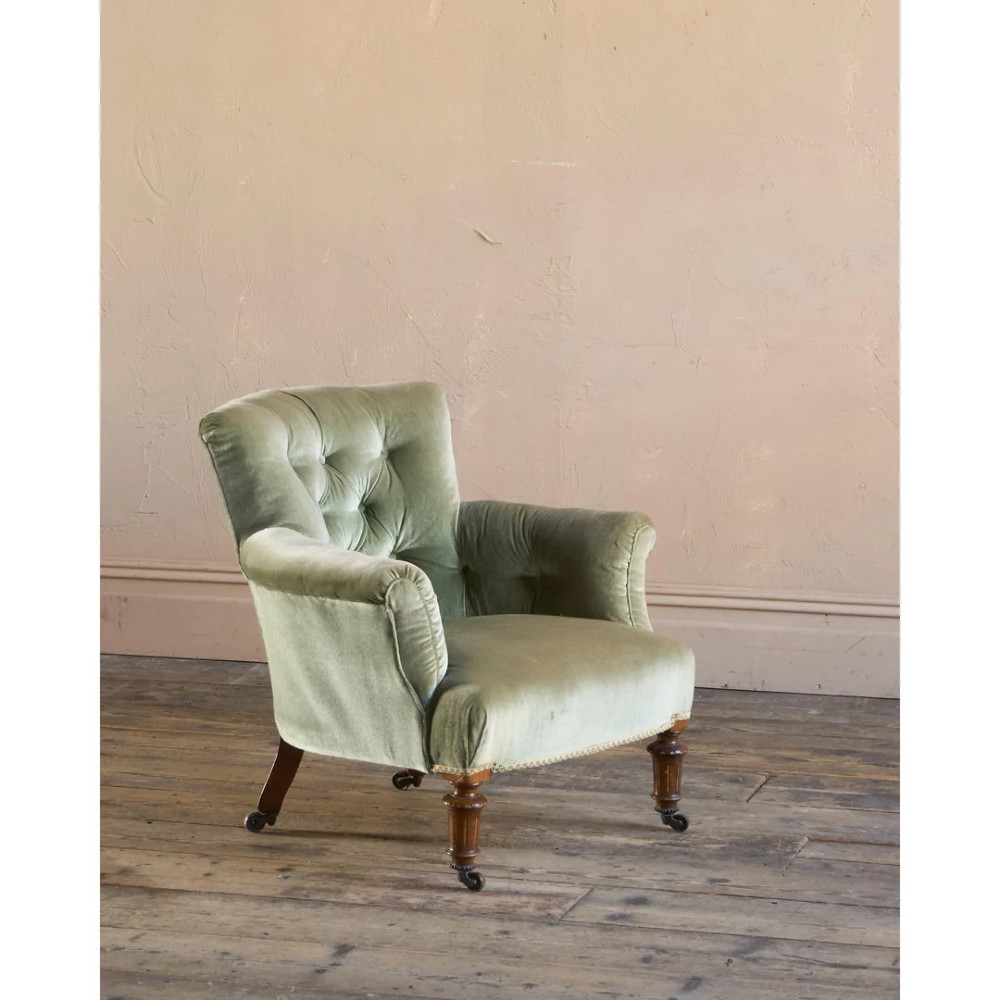 A 19th-century Victorian low armchair upholstered in light sage green velvet with a button-back design and turned wooden front legs on brass castors. View VI