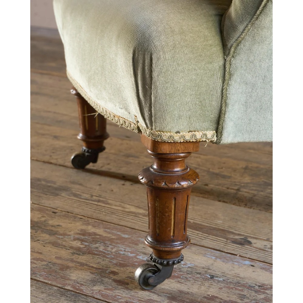 A 19th-century Victorian low armchair upholstered in light sage green velvet with a button-back design and turned wooden front legs on brass castors. View VIII