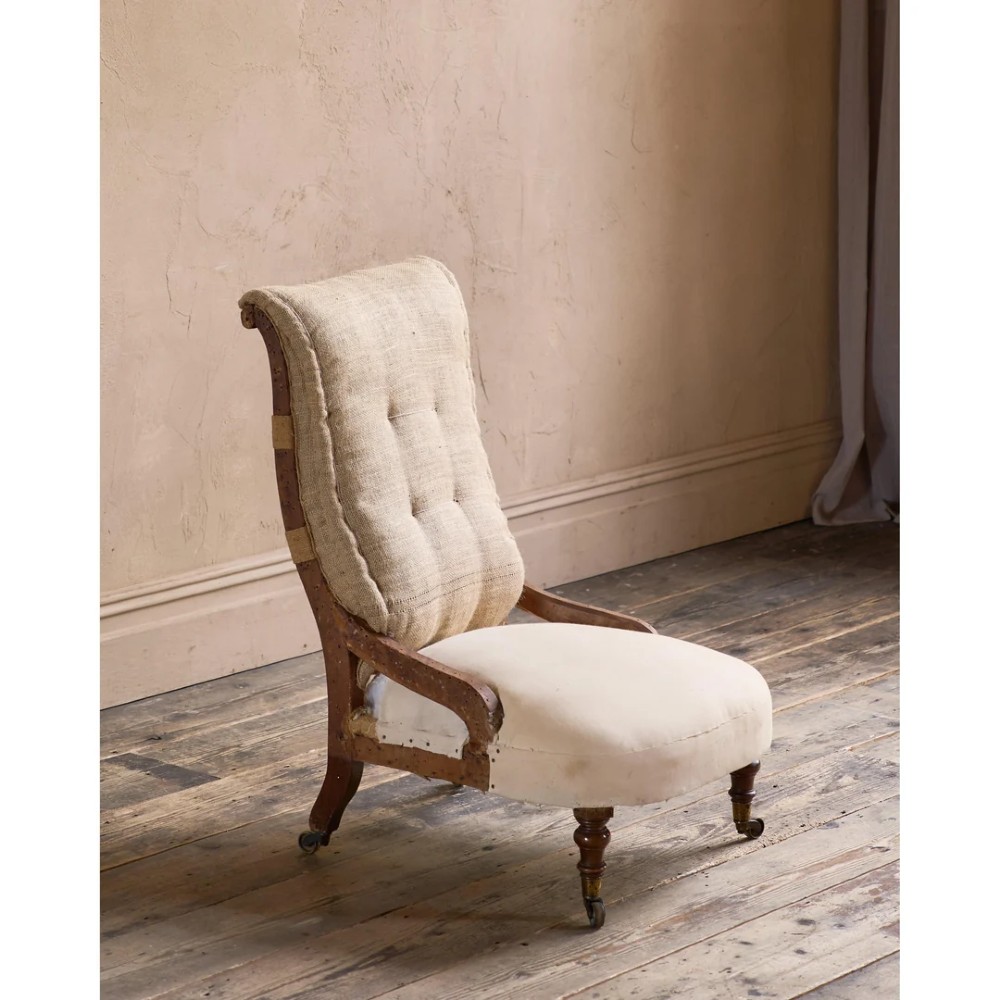 An early Victorian Howard and Sons low armchair shown in calico and hessian lining with turned front legs and brass castors.