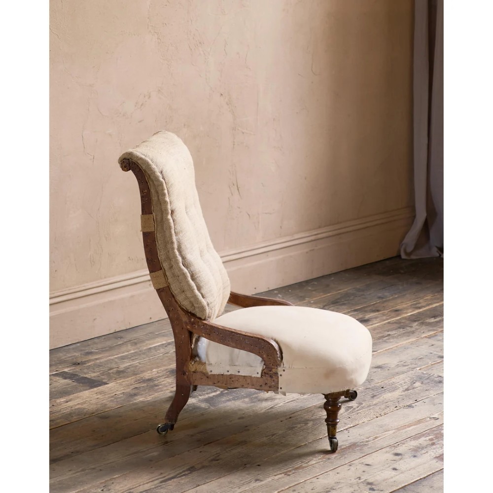 An early Victorian Howard and Sons low armchair shown in calico and hessian lining with turned front legs and brass castors. View V