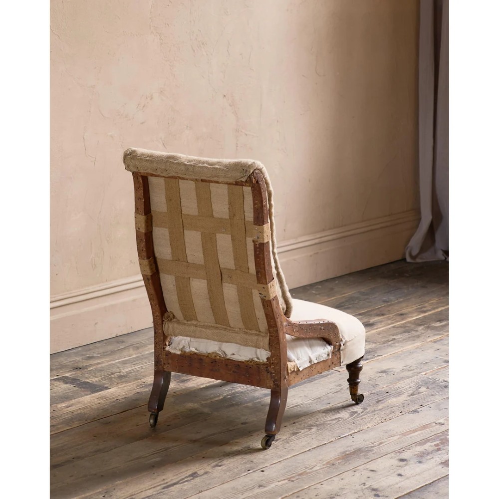 An early Victorian Howard and Sons low armchair shown in calico and hessian lining with turned front legs and brass castors. View VI