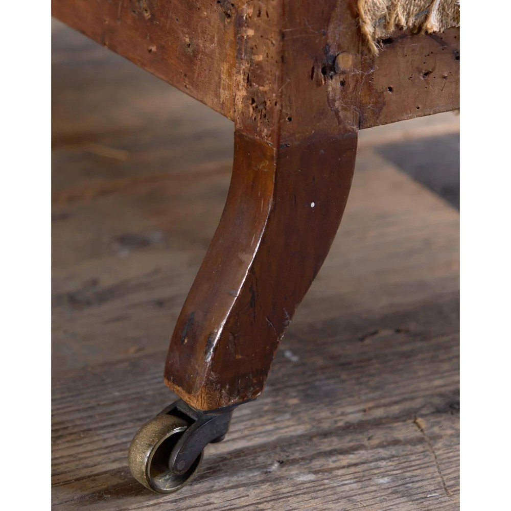 An early Victorian Howard and Sons low armchair shown in calico and hessian lining with turned front legs and brass castors. View IX
