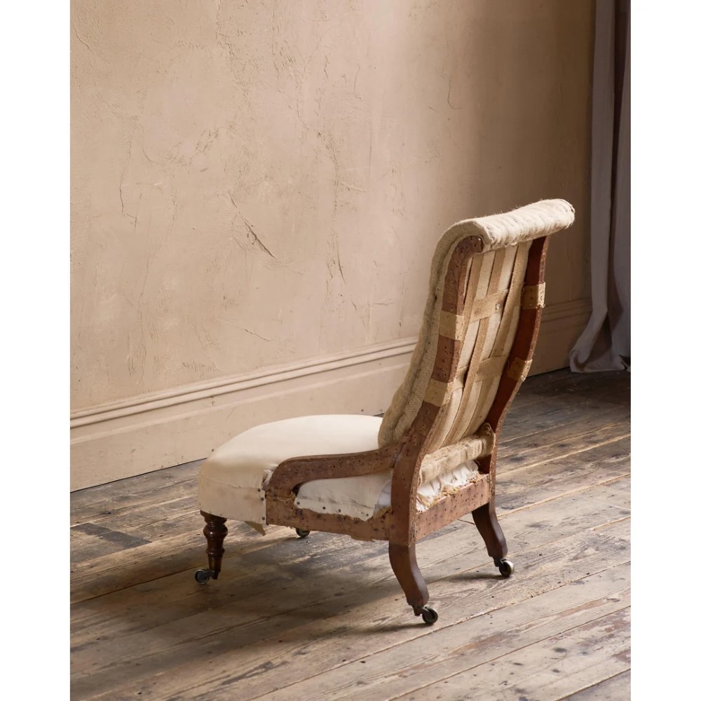 An early Victorian armchair featuring turned front legs on brass castors and hessian upholstery over a tufted backrest. View II