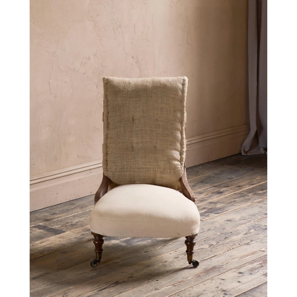 An early Victorian armchair featuring turned front legs on brass castors and hessian upholstery over a tufted backrest. View III