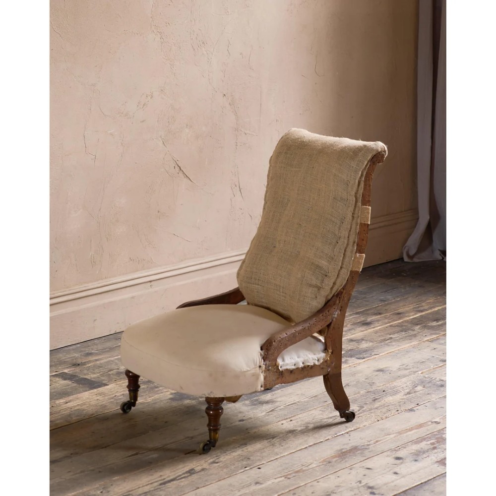 An early Victorian armchair featuring turned front legs on brass castors and hessian upholstery over a tufted backrest. View IV