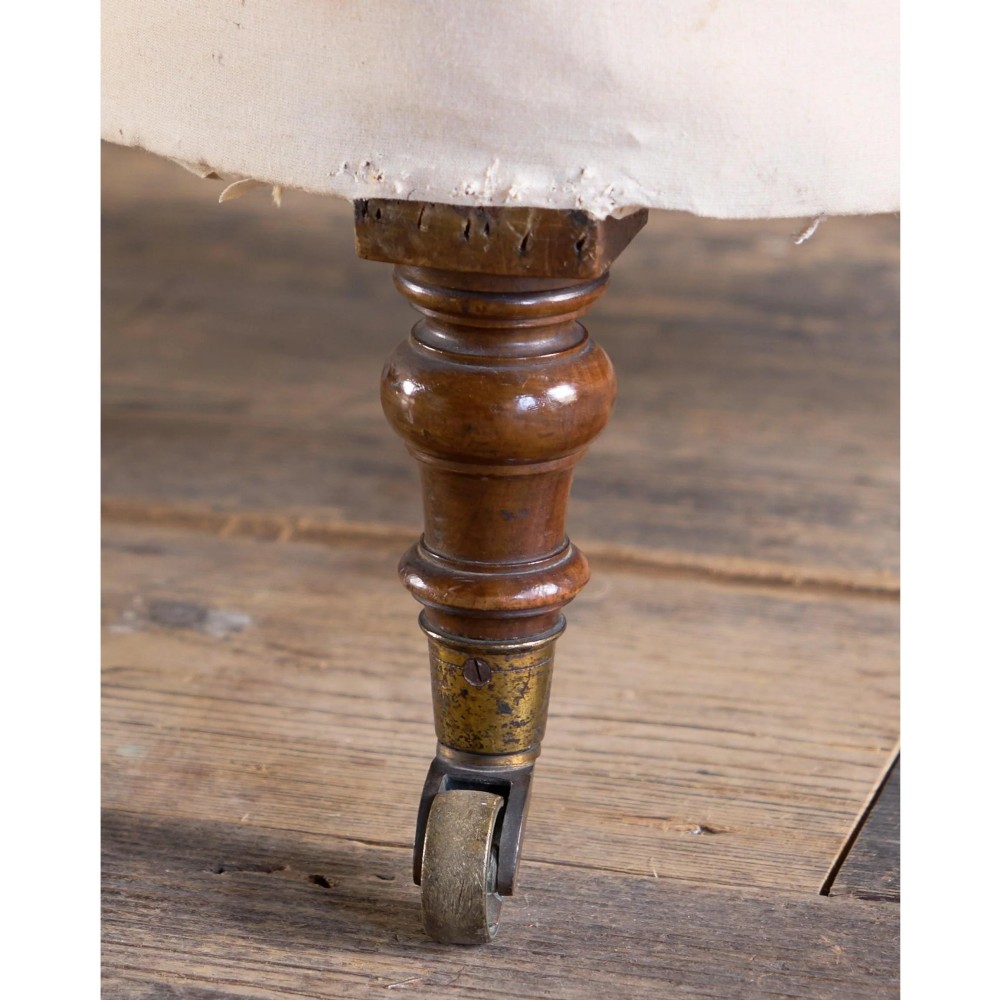 An early Victorian armchair featuring turned front legs on brass castors and hessian upholstery over a tufted backrest. View X