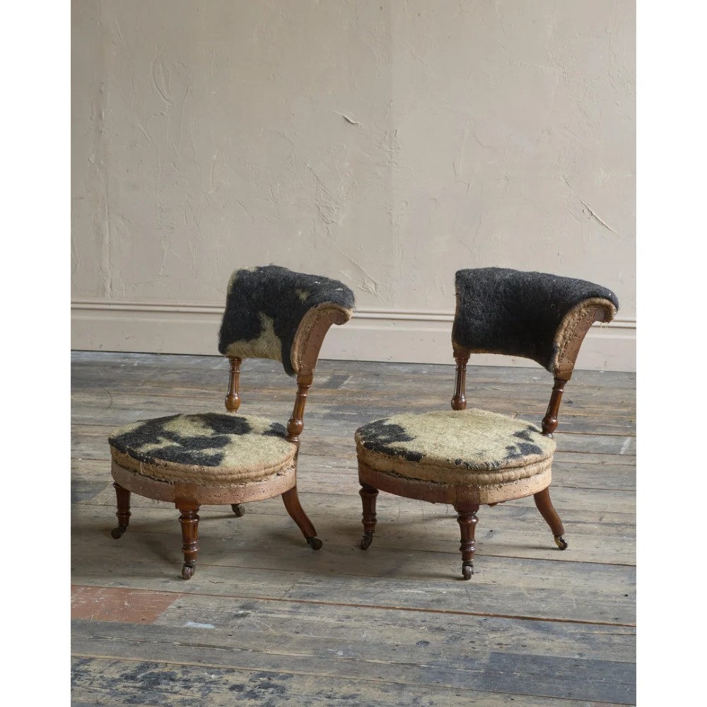 A pair of antique Victorian low-seated nursing chairs featuring rounded seat frames, turned front legs on brass castors, and exposed inner upholstery stuffing. View II