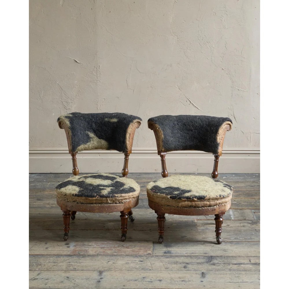A pair of antique Victorian low-seated nursing chairs featuring rounded seat frames, turned front legs on brass castors, and exposed inner upholstery stuffing. View III