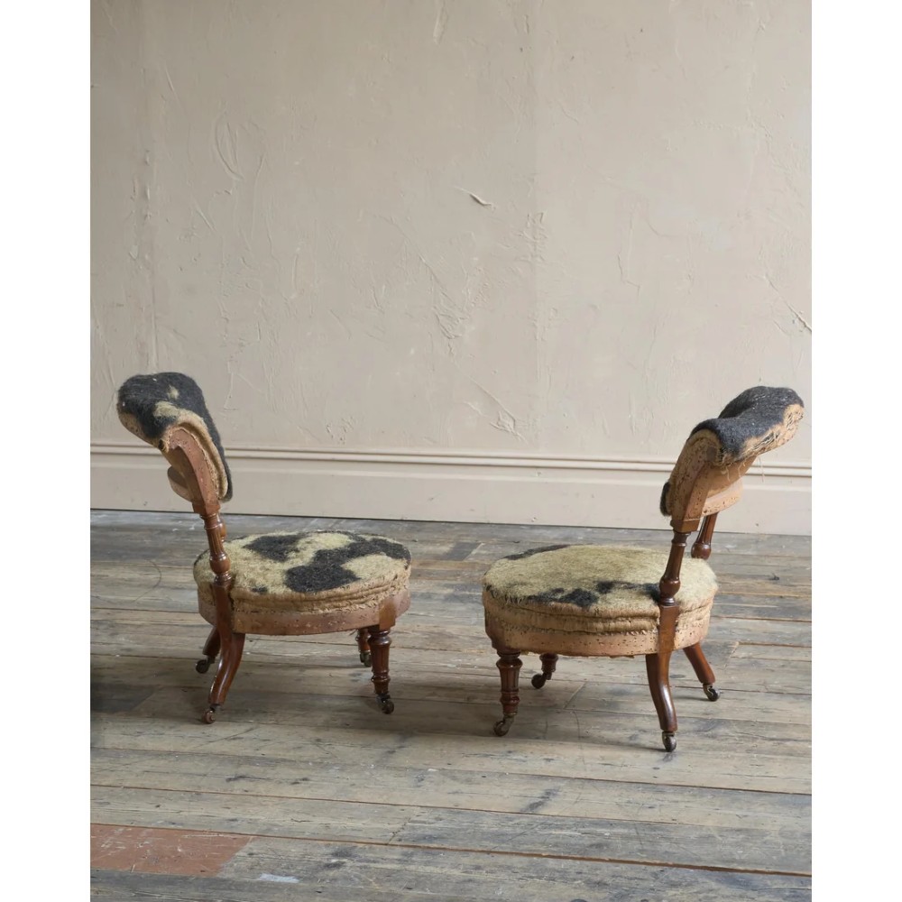 A pair of antique Victorian low-seated nursing chairs featuring rounded seat frames, turned front legs on brass castors, and exposed inner upholstery stuffing. View IV