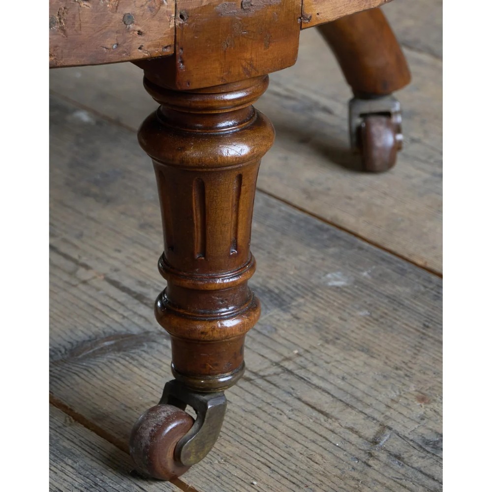 A pair of antique Victorian low-seated nursing chairs featuring rounded seat frames, turned front legs on brass castors, and exposed inner upholstery stuffing. View V