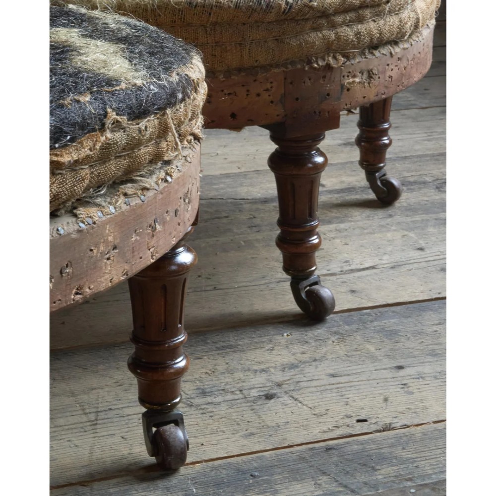 A pair of antique Victorian low-seated nursing chairs featuring rounded seat frames, turned front legs on brass castors, and exposed inner upholstery stuffing. View VI