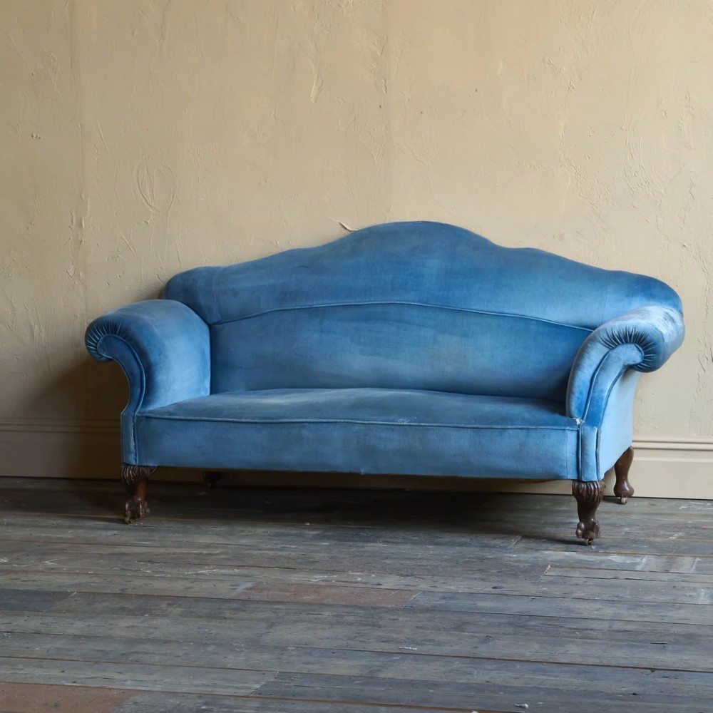 An antique blue velvet upholstered sofa featuring a curved back, rolled arms, and carved dark wooden cabriole legs with ball and claw feet on castors. View III