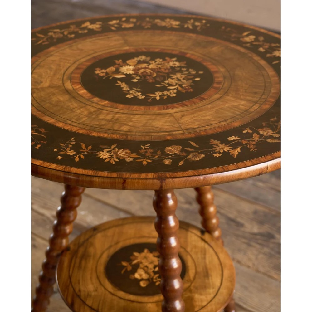 A circular warm brown wooden side table featuring floral marquetry inlays on the tabletop and lower shelf, supported by four bobbin-turned legs. View III
