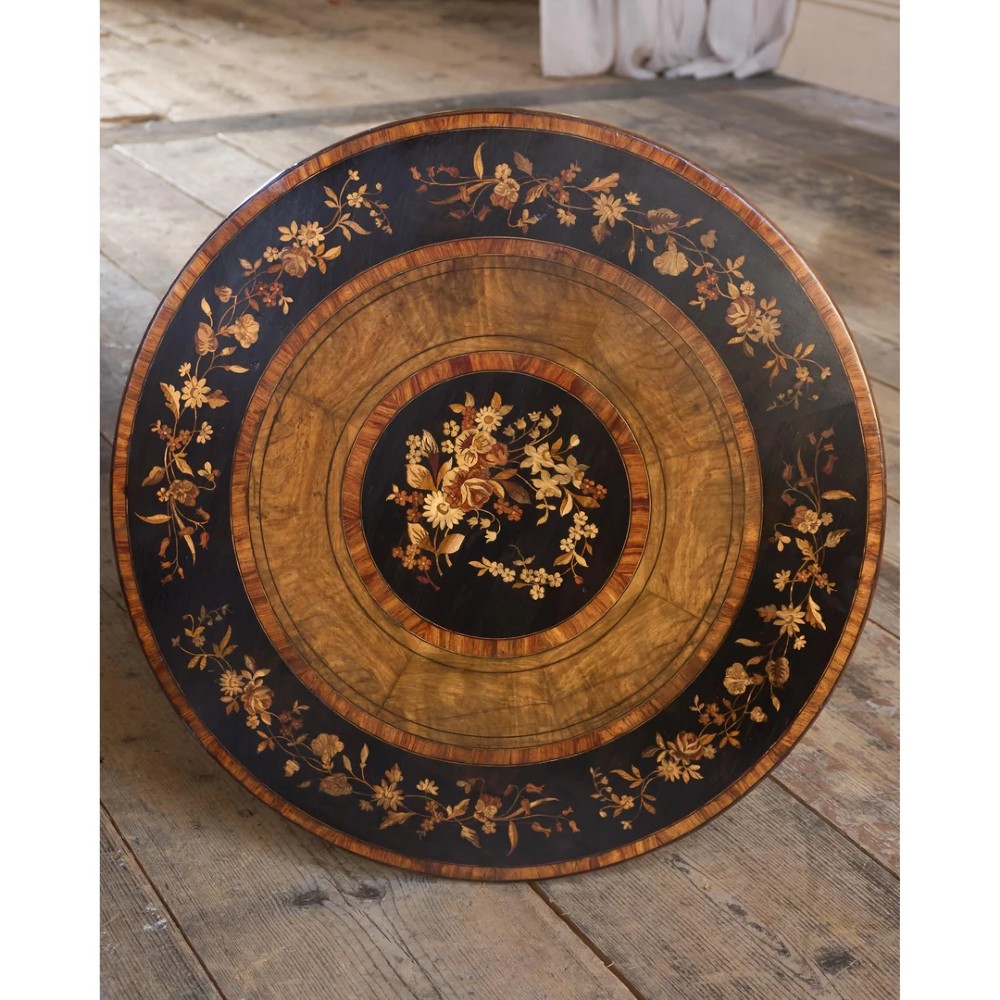A circular warm brown wooden side table featuring floral marquetry inlays on the tabletop and lower shelf, supported by four bobbin-turned legs. View VI