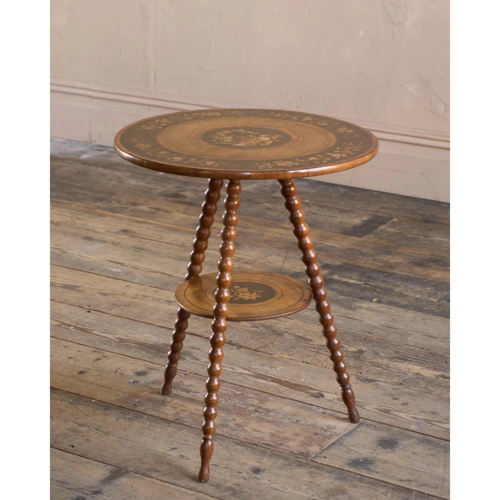 A circular warm brown wooden side table featuring floral marquetry inlays on the tabletop and lower shelf, supported by four bobbin-turned legs.