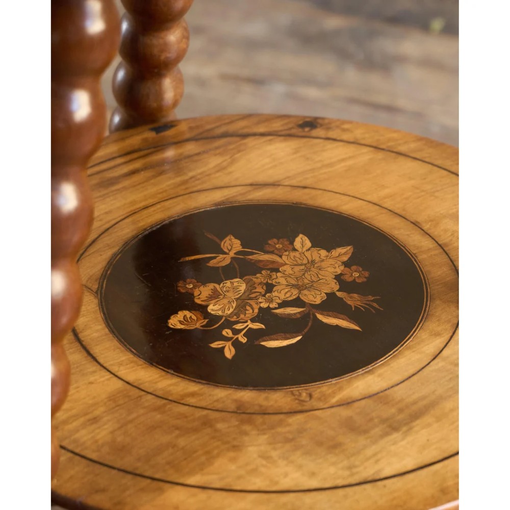 A circular warm brown wooden side table featuring floral marquetry inlays on the tabletop and lower shelf, supported by four bobbin-turned legs. View IX