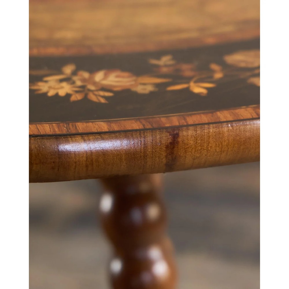A circular warm brown wooden side table featuring floral marquetry inlays on the tabletop and lower shelf, supported by four bobbin-turned legs. View X