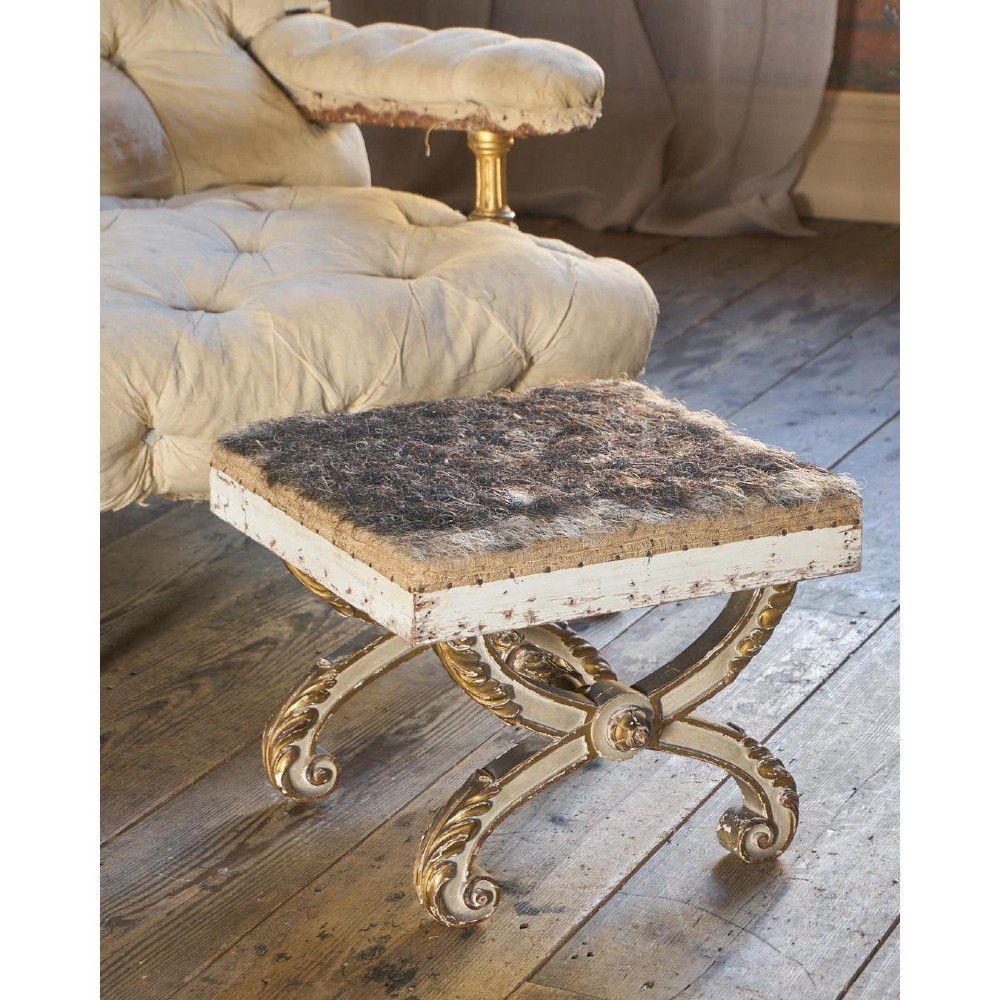 An antique curule X-frame footstool featuring carved scroll legs in grey paint and gilded finish with an upholstered top base. View II