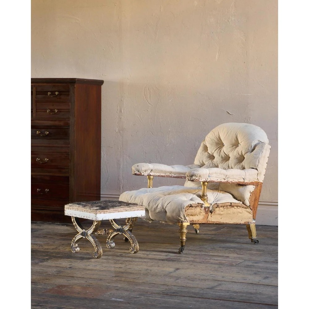 An antique curule X-frame footstool featuring carved scroll legs in grey paint and gilded finish with an upholstered top base. View III