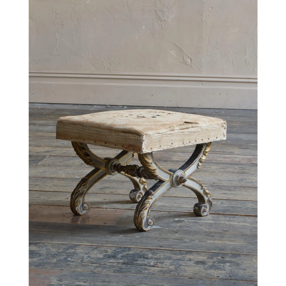 An antique curule X-frame footstool featuring carved scroll legs in grey paint and gilded finish with an upholstered top base. View IV