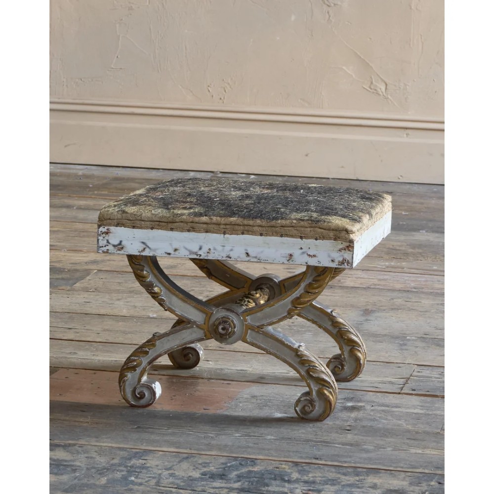 An antique curule X-frame footstool featuring carved scroll legs in grey paint and gilded finish with an upholstered top base. View VI